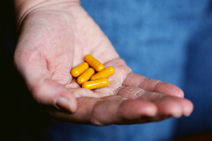 Senior holding five orange capsule pills in their hand.