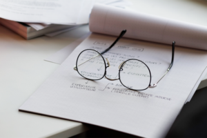 Eyeglasses on top of a notepad with work notes written on it.