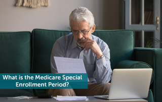 Elderly man sitting on a green couch looking at a piece of paper in front of an open laptop, wondering how Medicare Special Enrollment Period works.