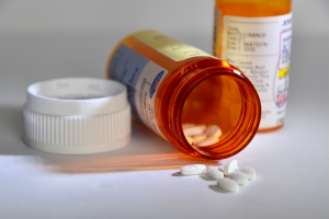 Two orange pill bottles on a white counter, one with the cap off with white pills spilled onto counter. 