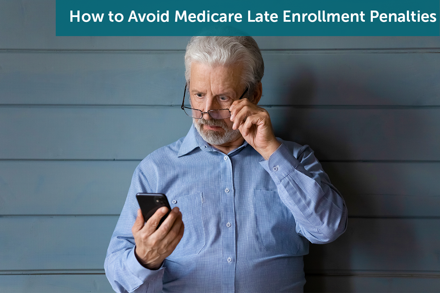 Senior man in a blue shirt looking at his cellphone, tilting his reading glasses in surprises as he looks at his Medicare late enrollment penalties.