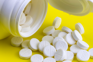 A white pill bottle spilling white pills on a yellow table. 