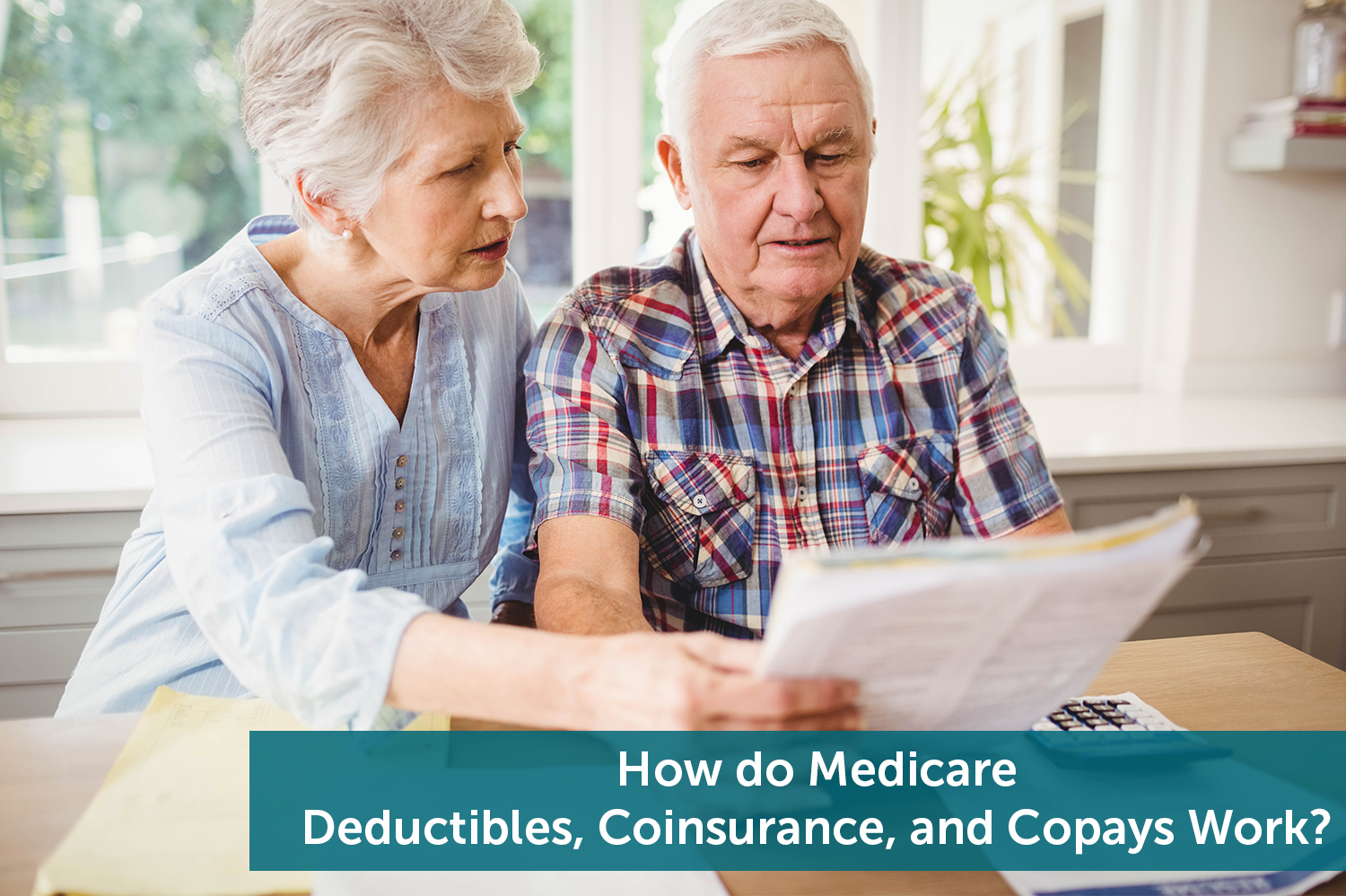 A senior man and senior woman looking over their bills for their Medicare deductibles and copays on a gray couch.