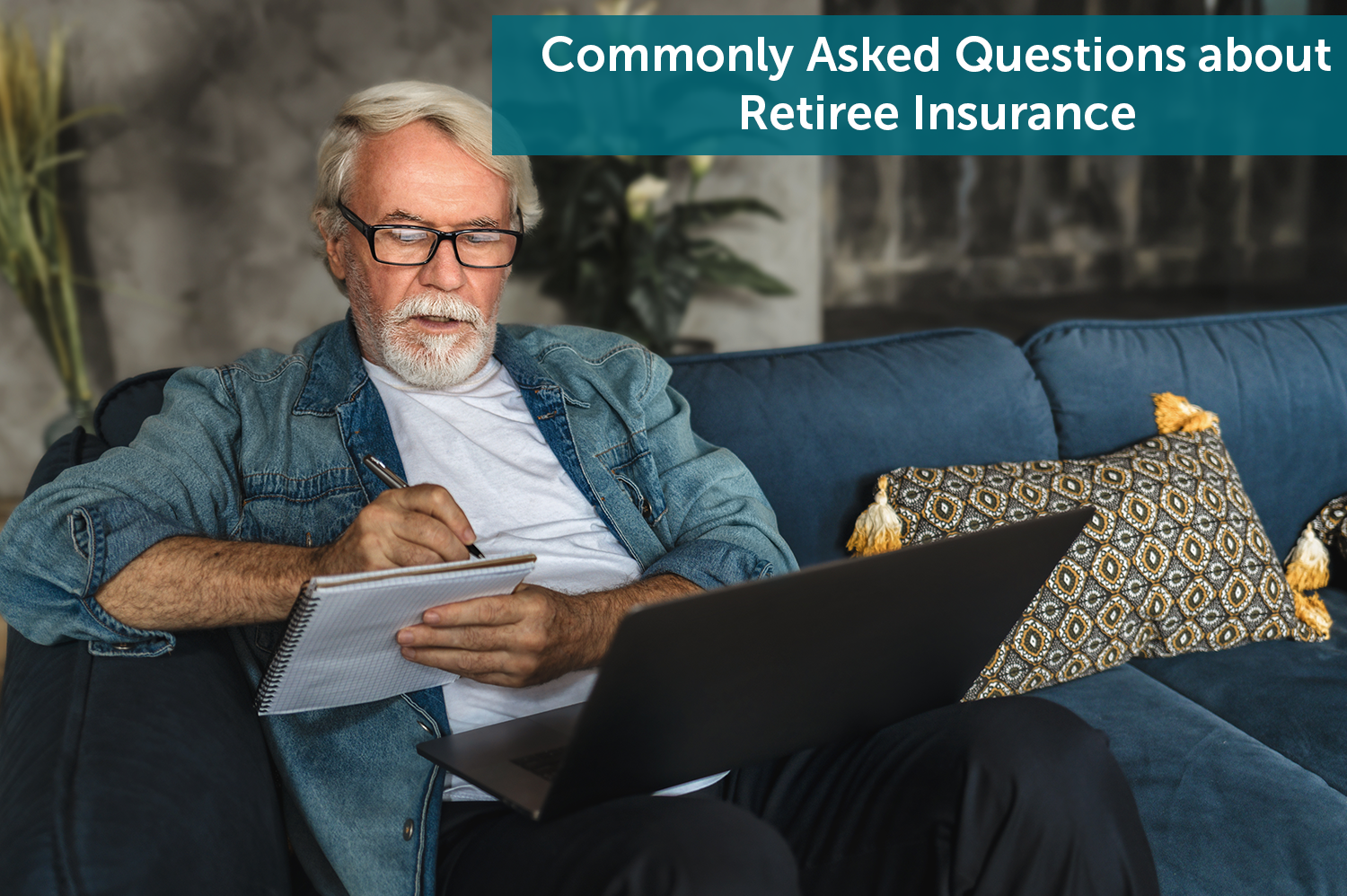 White senior man, sitting on a green couch with a laptop in his lap, writing down retiree insurance questions in a notebook.