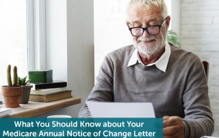 White senior man with beard sitting at table next to window, reading his Medicare Annual Notice of Change letter.