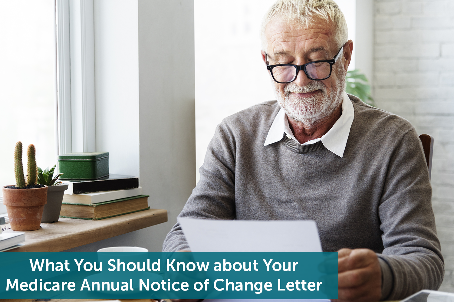 White senior man with beard sitting at table next to window, reading his Medicare Annual Notice of Change letter.